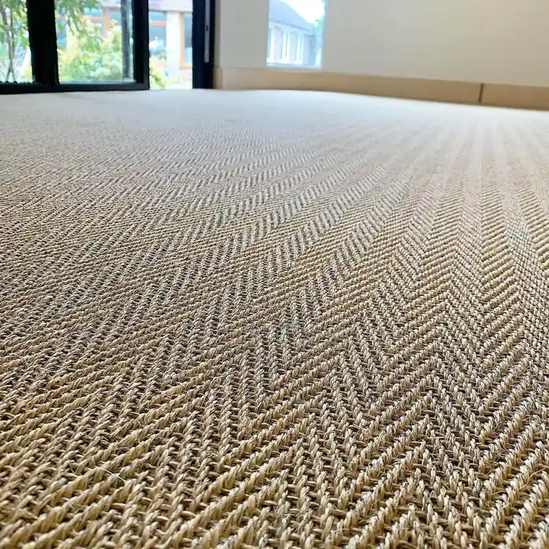 Low-angle close-up of a textured herringbone sisal carpet in a bright room